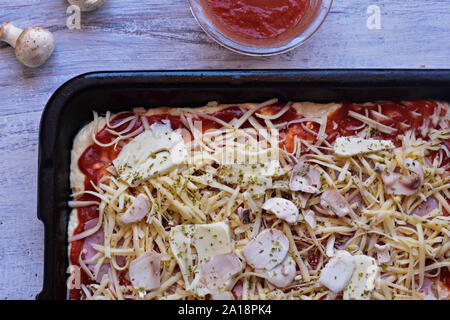 La pâte à pizza avec sauce tomate, fromage râpé, champignons et Mozzarella au fond en bois clair/ couverts/ fond alimentaire Banque D'Images