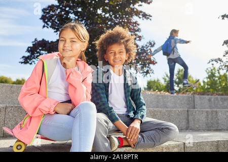 Portrait of cute girl sitting avec African boy et ils smiling at camera tout en vous reposant sur l'escalier extérieur Banque D'Images