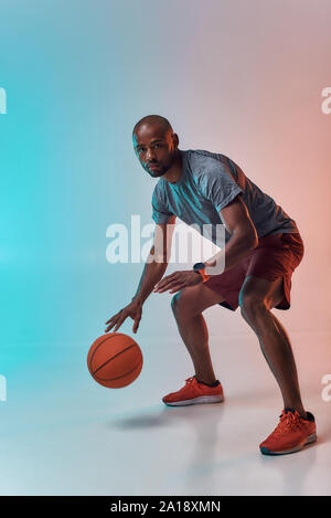 Prêt à gagner. Jeune homme africain plein de confiance dans des vêtements de sport jouant au basket-ball tout en se tenant sur un fond coloré. Mode de vie actif. Sport professionnel. Bannière Web Banque D'Images