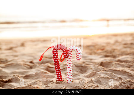 Noël arrière-plan avec des cannes de bonbon sur la plage de sable doré au coucher du soleil, concept de vacances saison - Image Banque D'Images