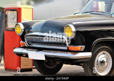 Partie frontale d'une vieille voiture noire vintage avec arrière-plan flou près de station d'essence rouge rétro Banque D'Images