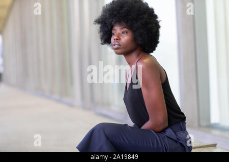 Jolie jeune femme africaine dans les rues de la ville, assis sur le banc Banque D'Images