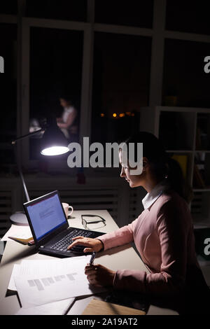 Young businesswoman sitting at the table à l'aide de son ordinateur portable et écrit sur papier elle travailler jusque tard en soirée à l'office de tourisme Banque D'Images