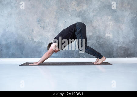 Young man working out, debout dans le yoga chien tête en bas adho mukha svanasana, posent, l'asana de surya namaskar, séquence complexe Soleil Yoga Banque D'Images