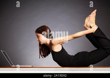 Woman in yoga pose arc avec ordinateur portable. Banque D'Images
