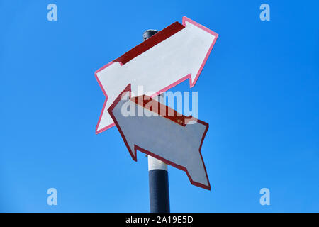 Flèche blanche signe avec deux flèches pointant dans des directions différentes, sur un ciel bleu. Banque D'Images