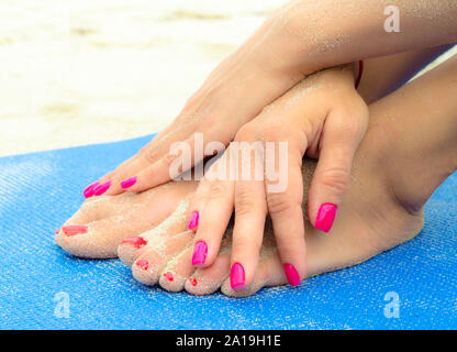 Femme avec les mains manucure rouge sur les jambes avec une pédicure avec du sable rouge sur les jambes et les mains sur un tapis bleu sur la plage Banque D'Images