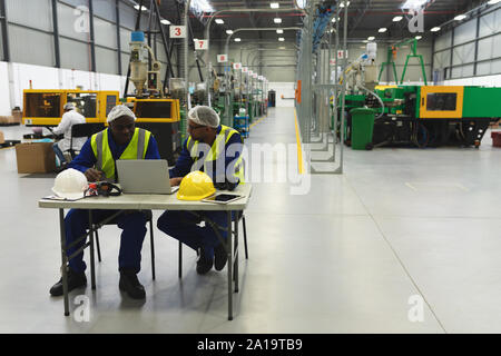 Les travailleurs d'usine mâle à l'aide d'ordinateur portable dans un entrepôt d'usine Banque D'Images