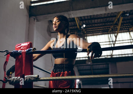 Boxer avec les yeux fermés s'appuyant sur des cordes en ring de boxe au club de boxe Banque D'Images