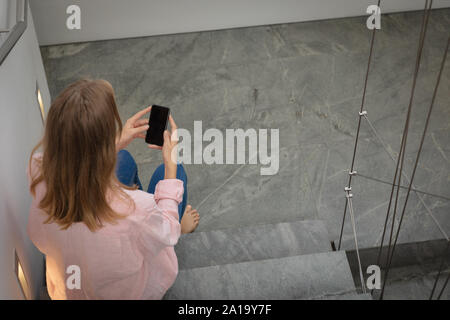 Young blonde woman sitting on stairs using smartphone Banque D'Images