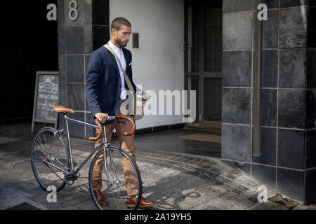 Jeune professionnel homme marchant avec une tasse de café wheeling un vélo Banque D'Images