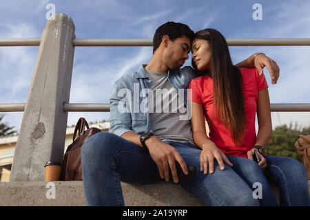 Young mixed race couple assis dehors sur un mur Banque D'Images