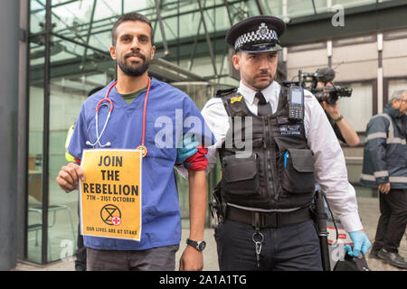 Londres, Royaume-Uni. 25 septembre 2019. Un professionnel de la santé en gommages médicaux et stéthoscope est escorté hors des lieux par un officier de la police métropolitaine lors d'une manifestation climatique extinction Rebellion devant le Department for Business, Energy & Industrial Strategy (BEIS) à Londres. La manifestation met en lumière la crise de santé publique imminente causée par le changement climatique. L’activiste porte une pancarte jaune indiquant « REBELLION 7TH - 21ST OCTOBER NOS VIES SONT EN JEU » avec le logo extinction Rebellion. Les médias et autres observateurs sont présents. Penelope Barritt/Alamy Live News Banque D'Images