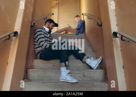 Les jeunes hommes assis sur un escalier et using smartphones Banque D'Images
