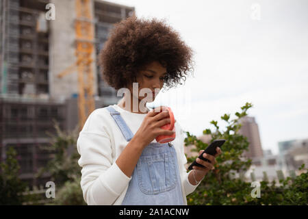 Jeune femme à boire le café sur un balcon using smartphone Banque D'Images