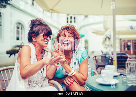 Image d'un deux happy senior women friends sitting in cafe de parler les uns avec les autres de boire du café, de rire et de pointer du doigt à quelqu'un. Banque D'Images