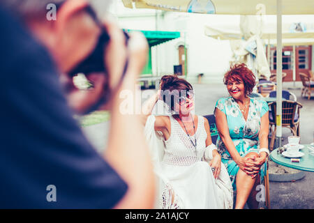 Le photographe prend une photo avec deux professionnels senior women sitting dans un café en plein air. Banque D'Images