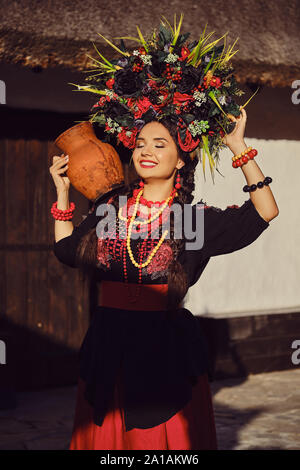 Fille brune dans un noir et rouge brodé ukrainien costume national authentique et d'une guirlande de fleurs est posant debout à la porte. Banque D'Images