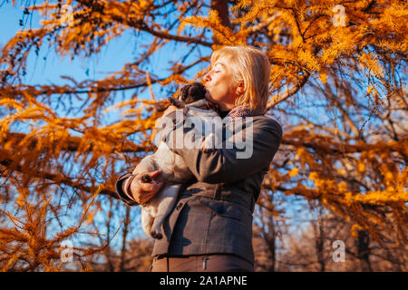 Pug dog Walking in autumn park. Happy woman hugging and kissing animal . Banque D'Images
