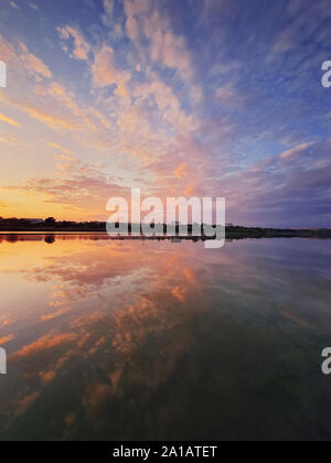 Shot verticale des nuages colorés moelleux reflétant le coucher du soleil sur la surface de l'eau du lac. Soirée calme et idyllique, scène avec beaucoup de nuages sur l'étang. Banque D'Images