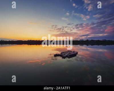 Fine art shot avec un vieux, rouillé châssis catamaran oublié sur l'étang. Paysage paysage paisible, avec fond de ciel coucher de soleil avec nuages colorés Banque D'Images