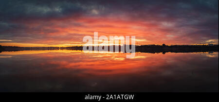Bold sunset panorama sur Delia lake, la Moldova. Crépuscule nuageux ciel et soleil rouge réflexion sur la surface de l'eau. Dramatique crépuscule paysage côtier. Banque D'Images