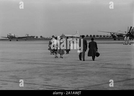 Un milieu xxe siècle vintage English Photographie noir et blanc montrant un groupe de personnes marchant sur un tarmac de l'aéroport vers l'attente de l'avion de Havilland Dove, l'immatriculation G-AKSK. Banque D'Images