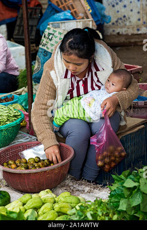 Jeune vendeur de légumes tenant son bébé au marché Phosi, Luang Prabang, Laos Banque D'Images