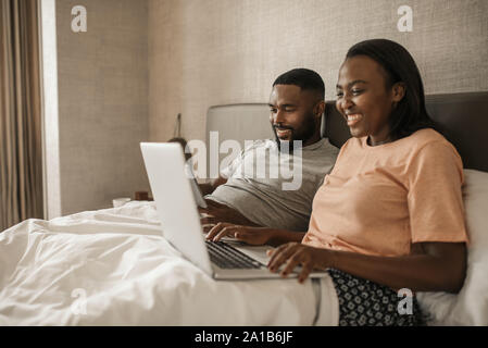 Couple à l'aide d'une tablette et l'ordinateur portable au lit Banque D'Images