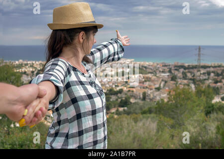 Une fille brune mène un gars par la main vous montrera la ville en face d'eux. Suivez-moi la notion de loisirs et de tourisme Banque D'Images