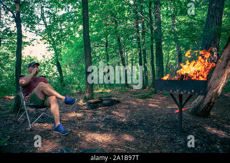 Homme assis en train de boire une bière président camp fire barbecue Banque D'Images