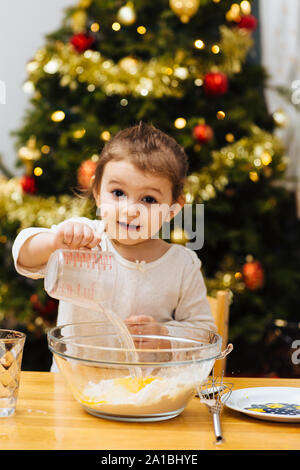 Happy little girl faire la pâte à crêpes en face d'un arbre de Noël Banque D'Images