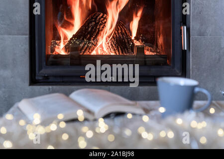 Hygge concept avec livre ouvert et tasse de thé près de cheminée à bois Banque D'Images