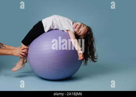 Petite fille est reposant sur un ballon de yoga, tandis que les mains tenant son repris blue Banque D'Images