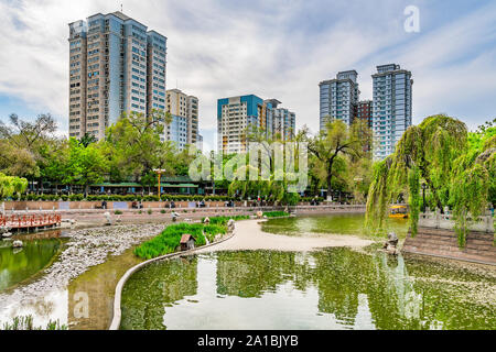 Urumqi Renmin Gongyuan People's Park Promenade au bord du lac avec des gratte-ciel à l'arrière-plan sur un ciel bleu ensoleillé Jour Banque D'Images