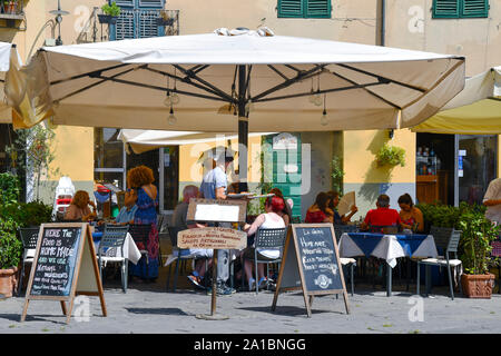 Restaurant en plein air sur la Piazza dell'Anfiteatro dans le centre de Lucca avec les gens et les touristes prenant le déjeuner sous des parasols en été, Toscane, Italie Banque D'Images
