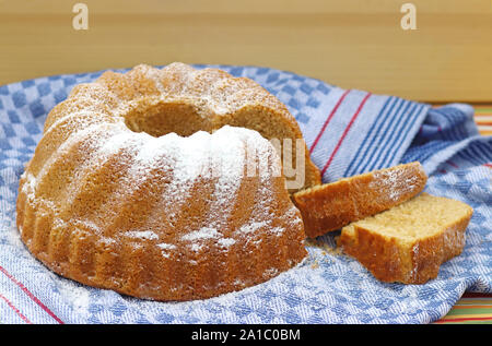 Gâteau bundt traditionnel avec deux tranches de gâteau sur une serviette de cuisine rétro, close-up avec un arrière-plan lumineux en bois et copy space Banque D'Images