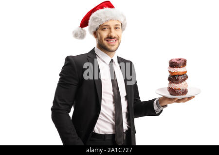 Jeune homme en costume holding a plate of chocolate donuts et wearing a Santa Claus hat isolé sur fond blanc Banque D'Images