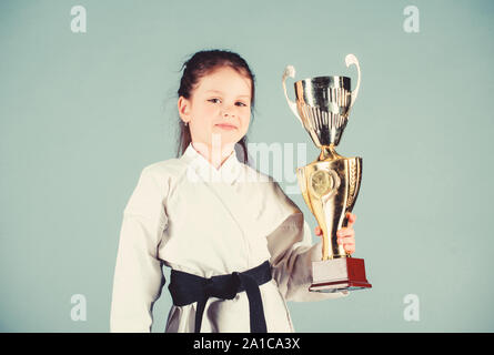 Petite fille gagnant dans gi sportswear. pratiquer le Kung Fu. enfance heureuse. sport succès en combat singulier. girl avec champion cup. Les arts martiaux et l'activité de l'énergie. knockout. Tout est possible. Banque D'Images