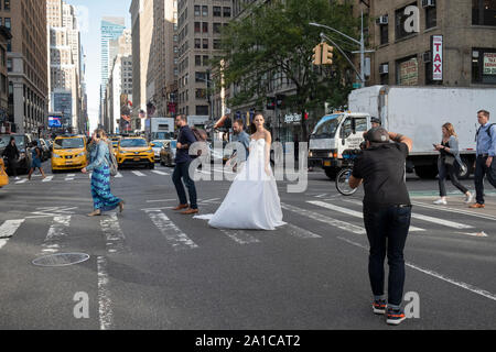 Un modèle d'une robe nuptiale pose pour des photos sur un coin de rue animée - 7th Ave. et West 29th Street - à Manhattan, New York City. Banque D'Images