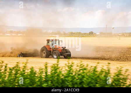 Tracteur labourer le champ dans le coucher du soleil avec des poussières dans l'air Banque D'Images