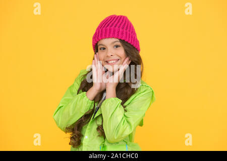 Choisissez entre plus mignonne et la plus branchée. Kid girl porter chapeau tricoté. Bonnet hiver accessoire. Des cheveux longs de fille fond jaune. Saison froide concept. Accessoire de mode d'hiver. Petit enfant portant chapeau chaud. Banque D'Images