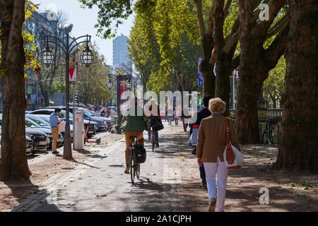 Les gens à pied et faire du vélo sur de belles pistes cyclables et trottoirs ombragés à Königsallee à Düsseldorf, Allemagne. Banque D'Images