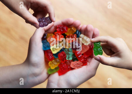 Une poignée d'ours gommeux doux et coloré, et deux enfants mains ramasser leur saveur préférée out Banque D'Images