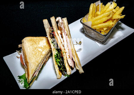 Un club sandwich grillé savoureux rempli de poulet grillé, salade et jambon de dinde servi avec frites Banque D'Images