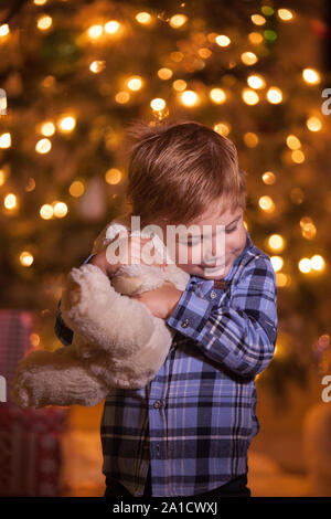 Little woman hugging son ours en peluche est en face de l'arbre de Noël Banque D'Images