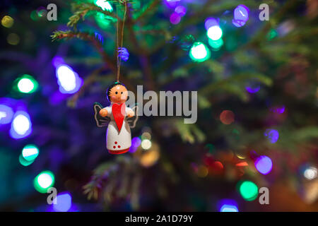 Jouet de Noël ange avec un cœur rouge dans les mains accroché sur l'arbre de Noël. Garland s'allume à l'arrière-plan sous forme de coeur Banque D'Images