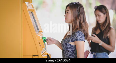 Deux jeunes femmes asiatiques retire de l'argent d'une banque à l'aide d'un distributeur de billets au centre commercial Banque D'Images