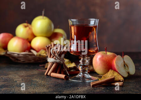 Verre de jus de pomme ou de cidre avec des pommes juteuses et des bâtons de cannelle sur une table de cuisine. Banque D'Images