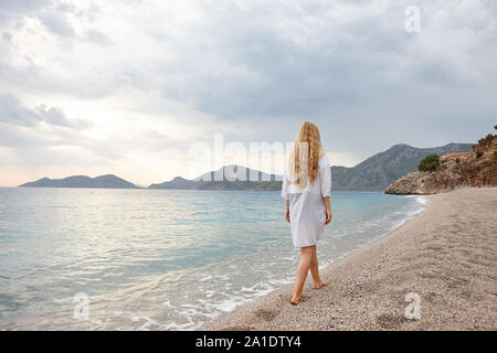 Jeune femme passant plage déserte sur le coucher du soleil Banque D'Images